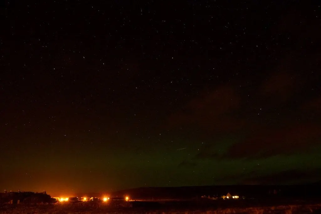 Green aurora over a dark Scottish coastline